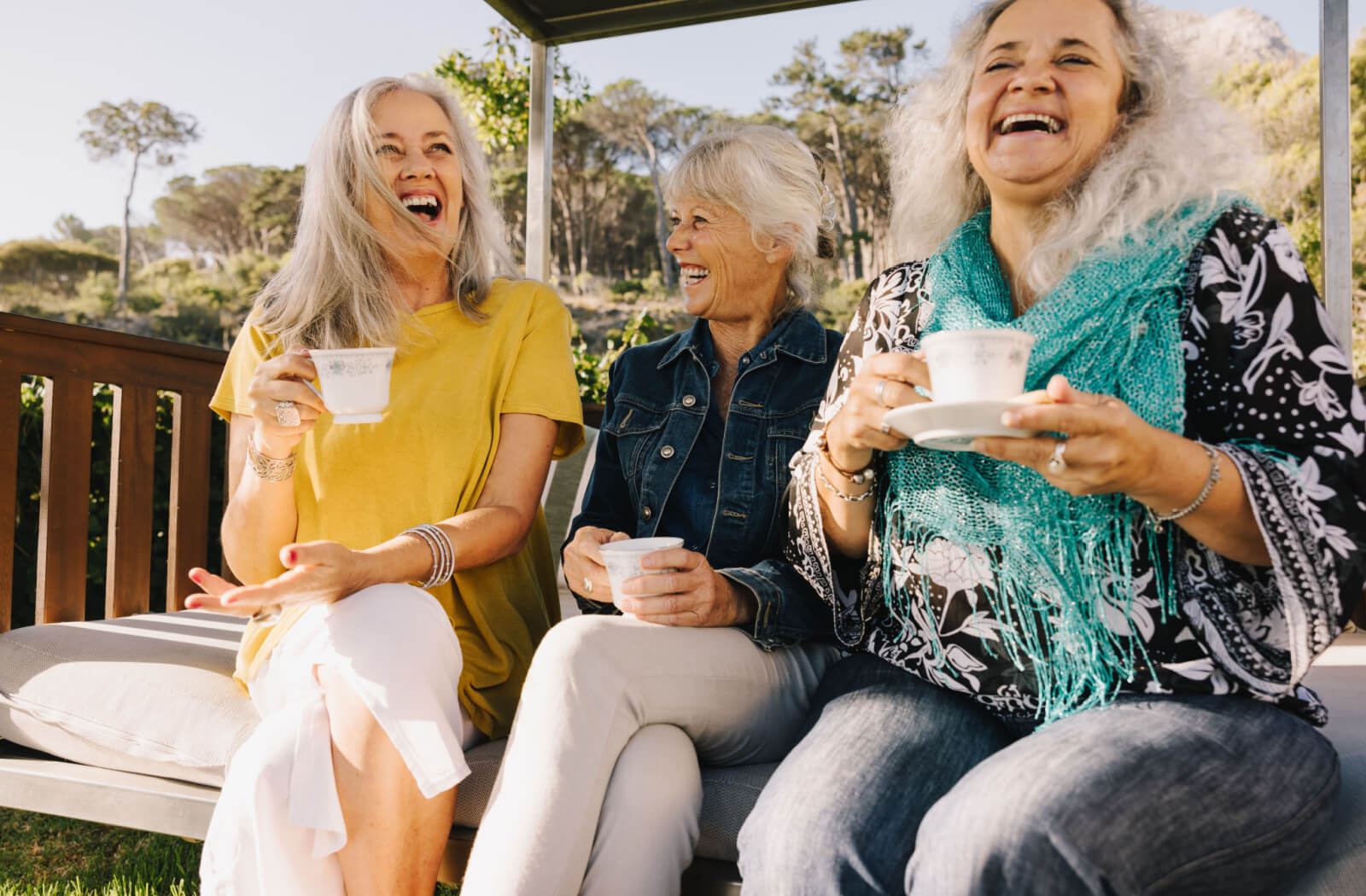 A group of senior women enjoying a cup of tea on an outdoor bench.