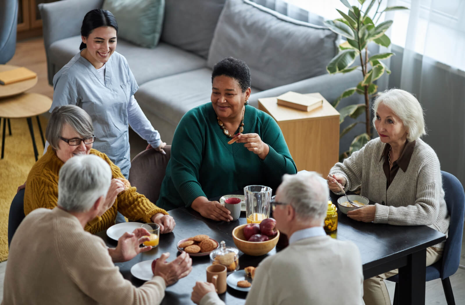 A group of seniors enjoying a conversation in the shared dining space of an assisted living centre.