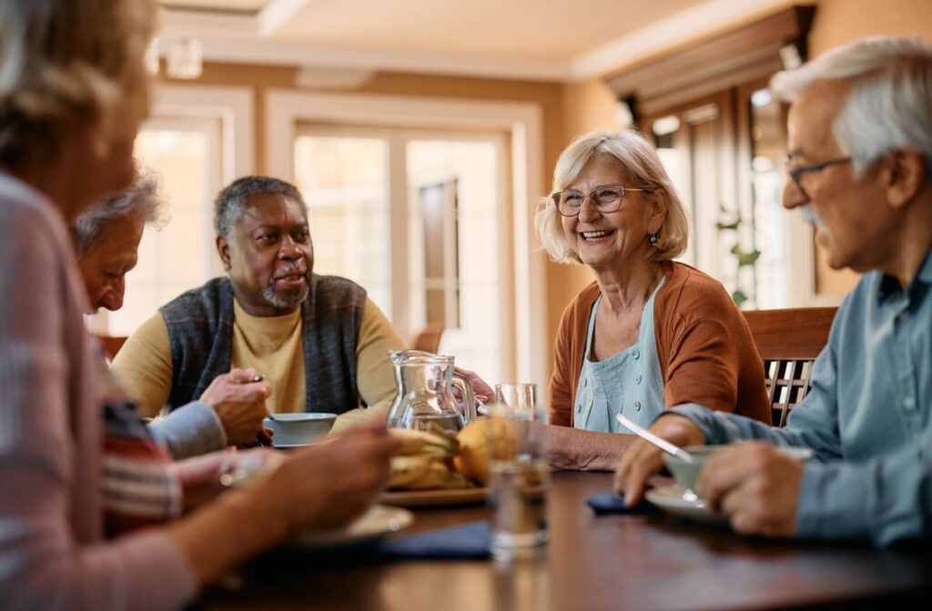 a group of seniors sit at a table eating and chatting in a senior living community's dining area